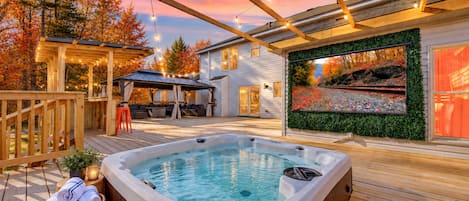 A hot tub on a wooden deck with a covered seating area and a wall-mounted aquarium.