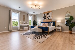 A bedroom with a bed, bedside tables, a desk, a chair, a large window, and a plant. - NEW! Indoor Lounge Pool Hot tub Glamping Karaoke (Tobyhanna)