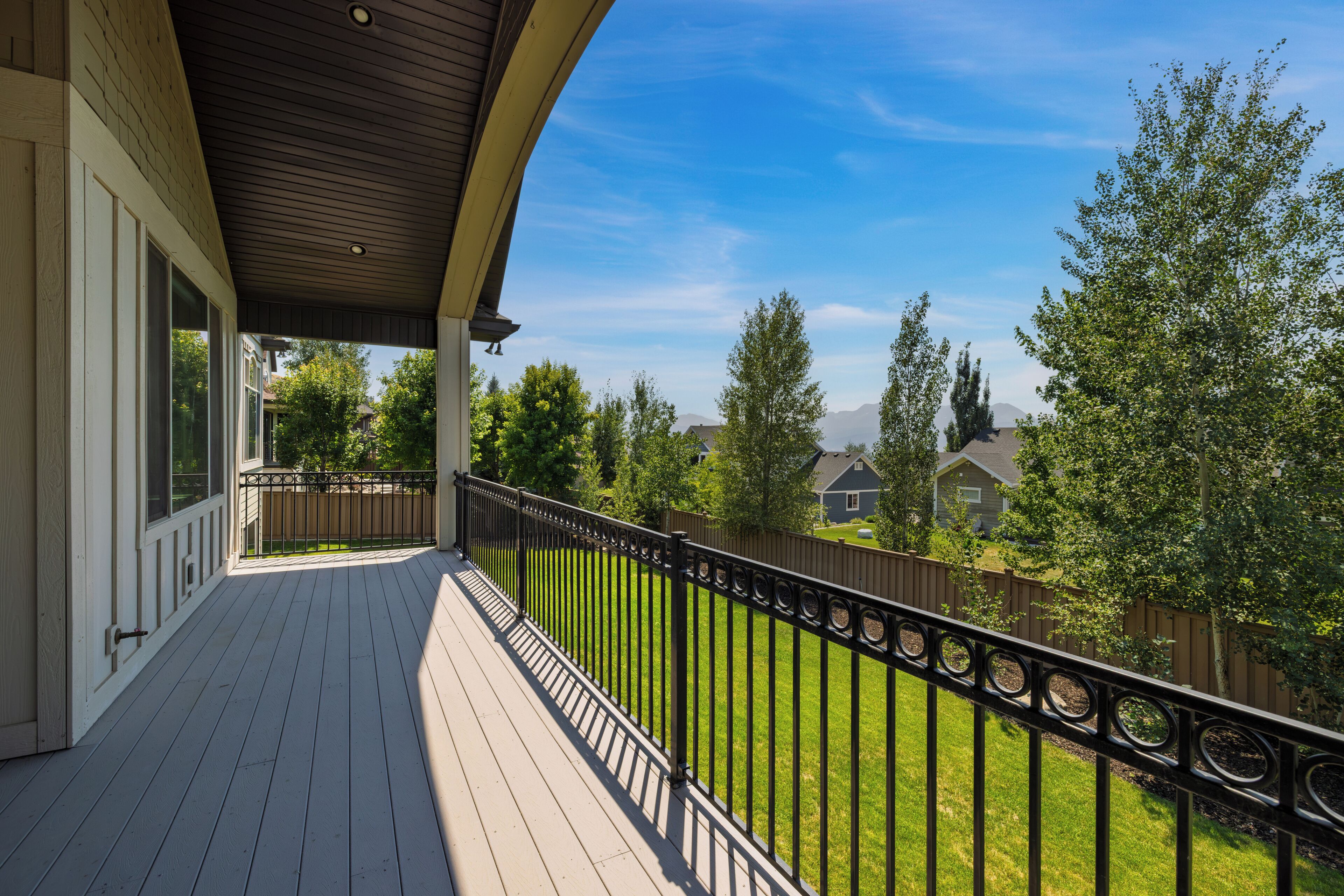 A covered outdoor deck with a railing, overlooking a well-maintained lawn and neighboring houses.