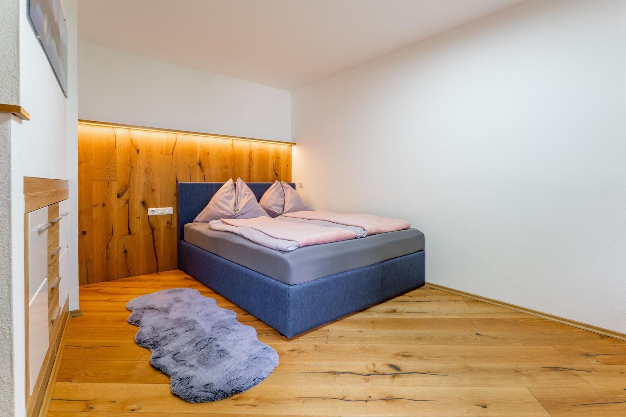Une chambre avec un lit intégré, un mur recouvert de panneaux en bois et un tapis en fourrure sur le sol.