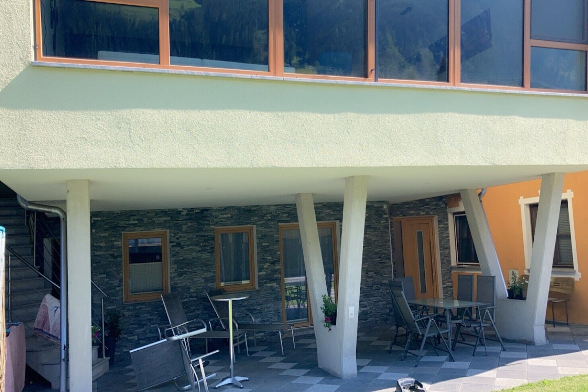 A covered outdoor area with stone walls, a table with chairs, and a staircase leading to an upper level.