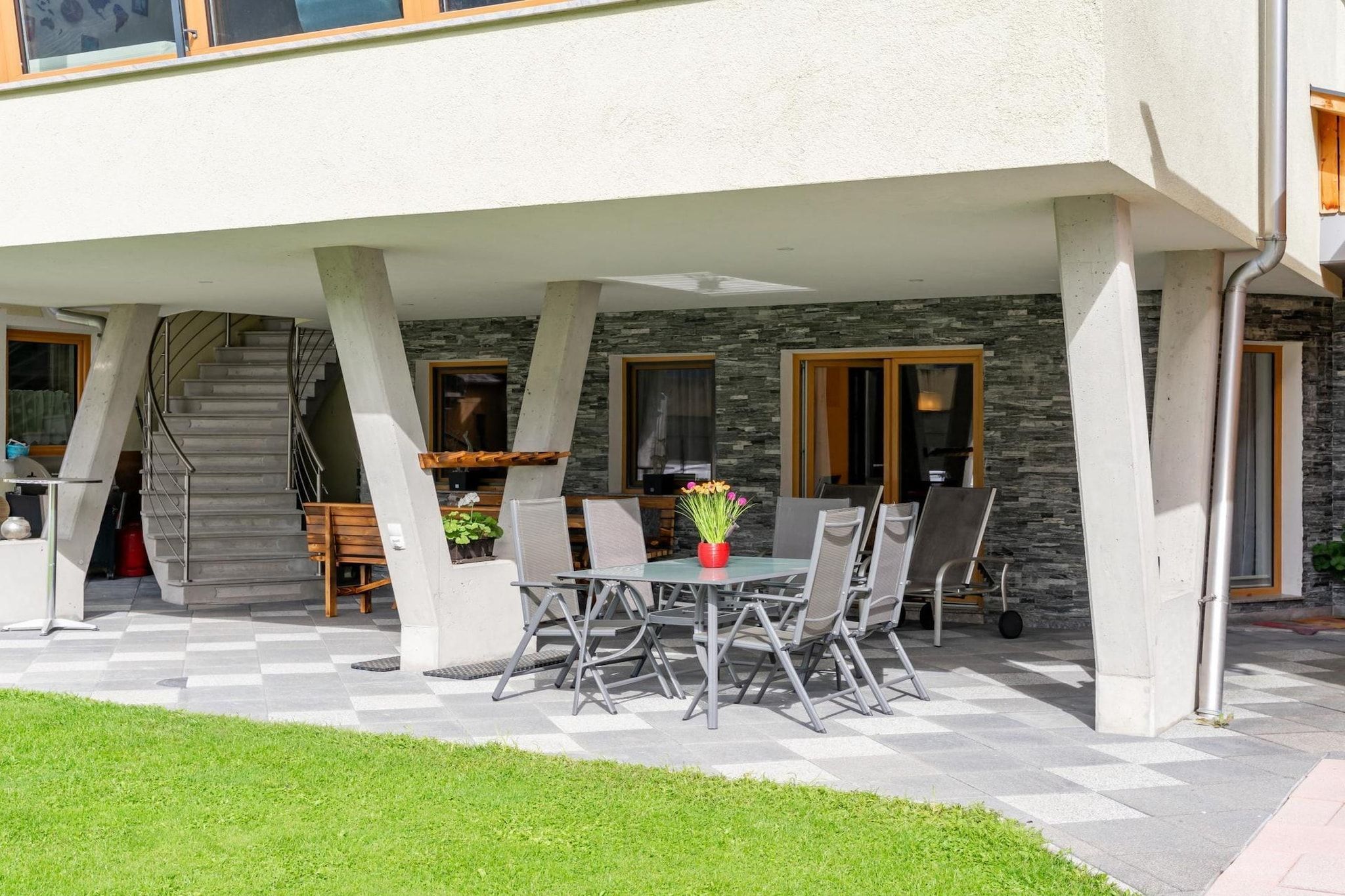 An outdoor patio with a table and chairs, a staircase, and a stone wall.