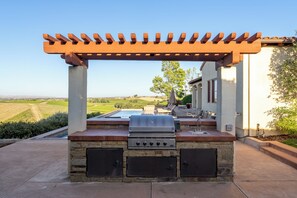 Cozinha externa com churrasqueira, espaço de armazenamento embutido e pérgola.