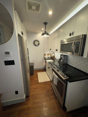 A modern kitchen with white cabinets, stainless steel appliances, a microwave, and a clock on the wall. - Delightful 2-bedroom apartment with AC in vibrant Brooklyn (Brooklyn)
