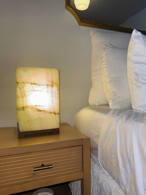 A bedside table with a lamp, a bed with white bedding, and a wall-mounted light fixture. - Delightful 2-bedroom apartment with AC in vibrant Brooklyn (Brooklyn)
