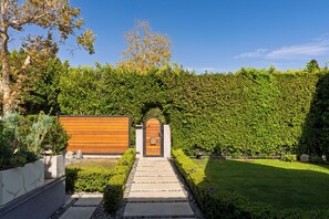 Un sendero conduce a un portón de madera, rodeado por un seto bien cuidado y un césped impecable.