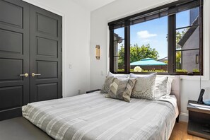 Quarto com cama, janela com vista para o exterior, porta e mesa de cabeceira com abajur.