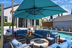 Uma área de estar moderna ao ar livre, com piscina, móveis azuis e um grande guarda-sol.