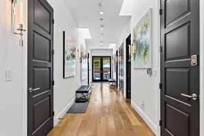 A hallway with dark doors, artwork on the walls, a bench, and a view into the outside. - Pool + Hot Tub + Firepit + BBQ | Walk to Melrose + The Grove | Crescent Peak (West Hollywood)