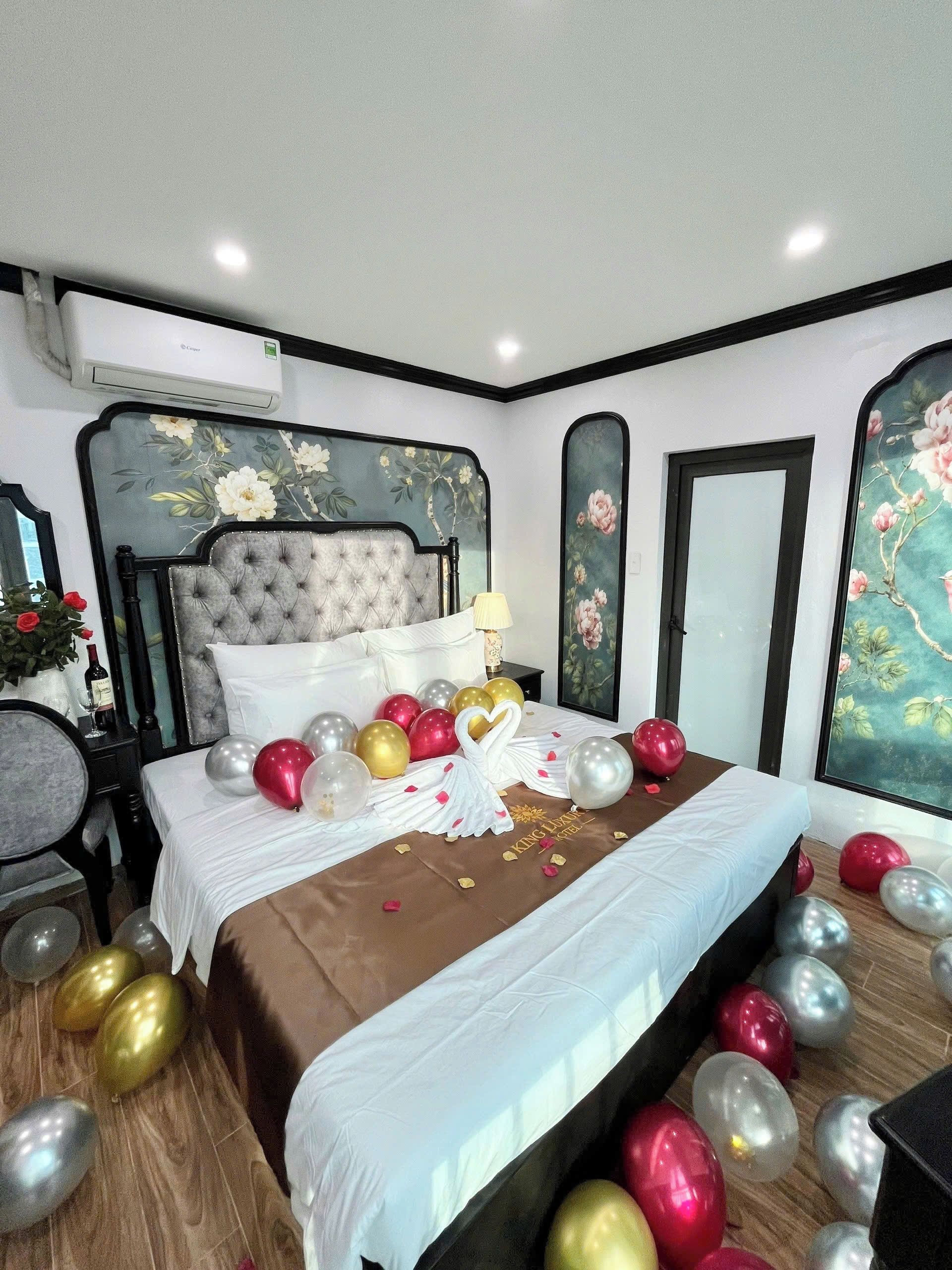 A hotel room with a large bed, a nightstand, a mirror, and a wall with floral wallpaper.