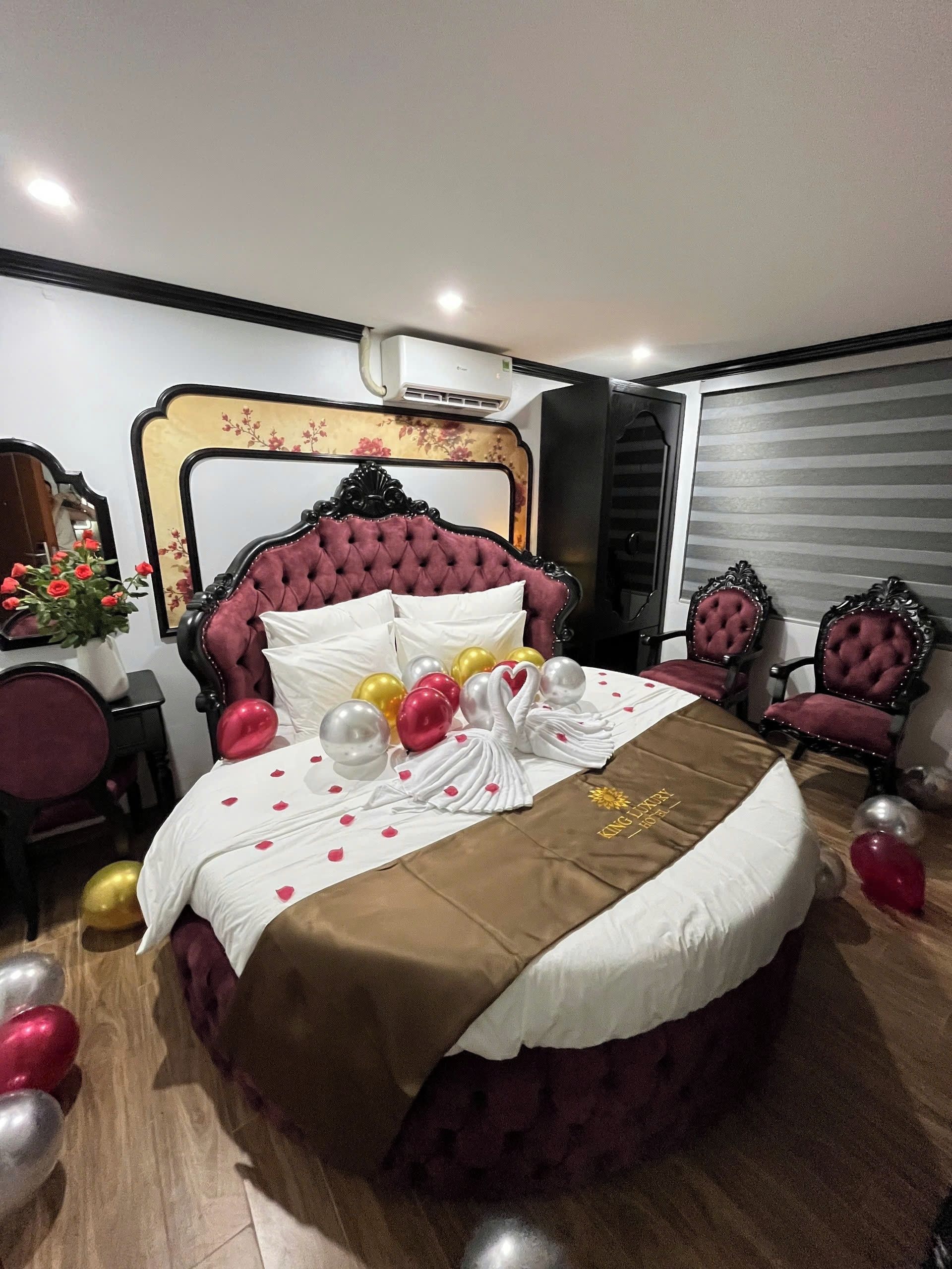 A bed with a tufted headboard, a white bedspread with red heart decorations, and a brown blanket.