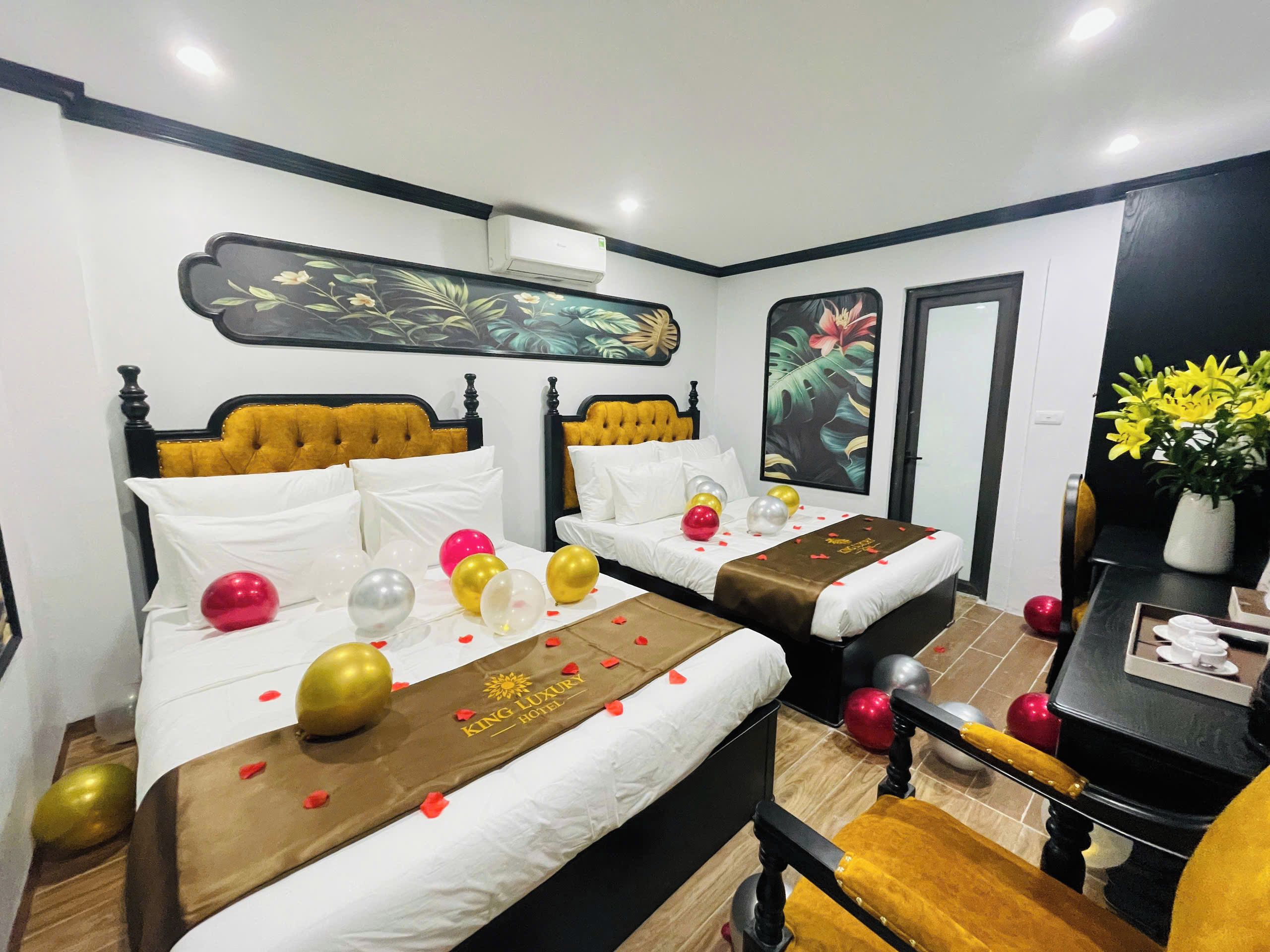 Habitación de hotel con dos camas, un escritorio y una silla. Hay globos y un ramo de flores sobre las camas.