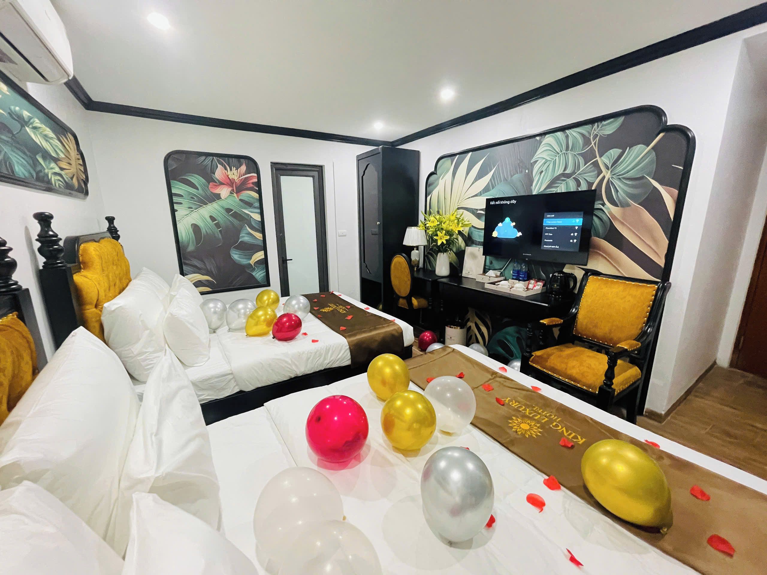 A hotel room with a bed, a desk with a computer, a chair, and a wall with a floral mural.