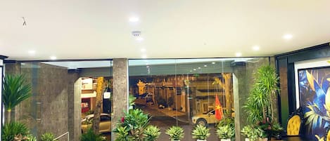A reception area with a glass partition, potted plants, and a seating area with yellow chairs.