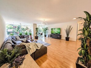 Ein geräumiges Wohnzimmer mit einer Sofagarnitur, einem Flachbildfernseher und mehreren Blumentöpfen.