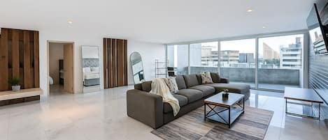 A modern living room with a sofa, coffee table, and a view of the city through large windows.
