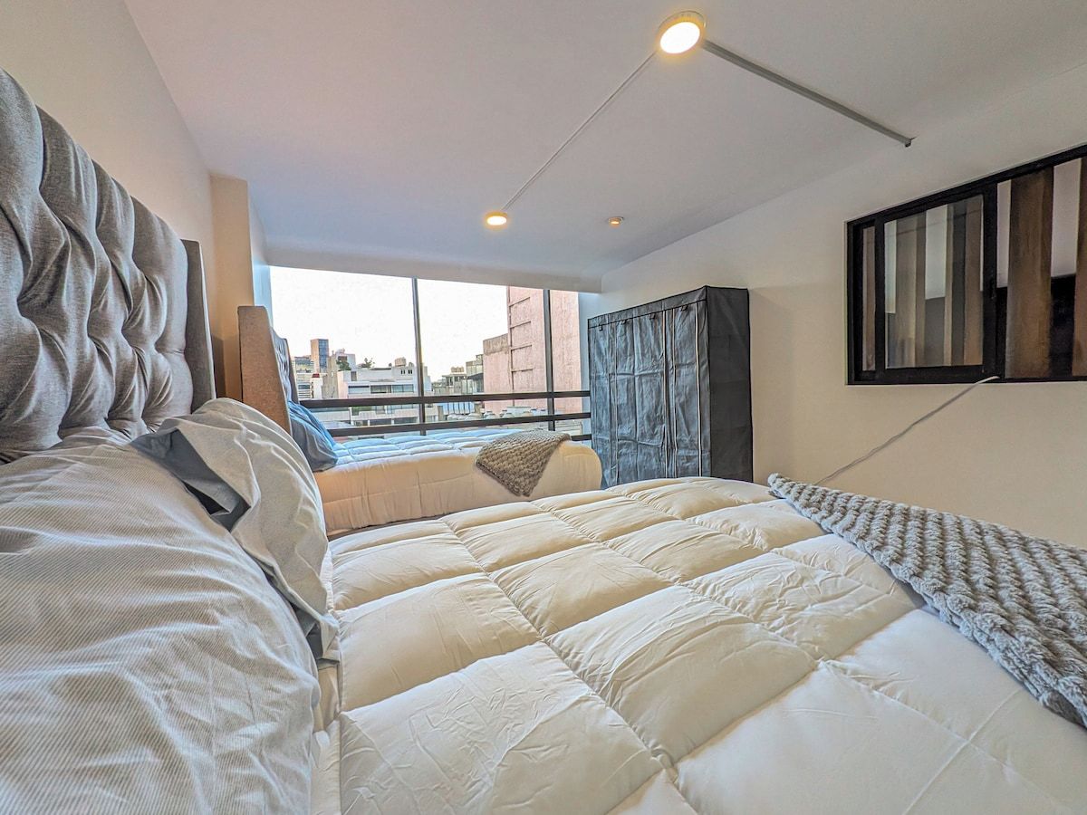 A modern bedroom with a large bed, a view of the city, and a window with curtains.