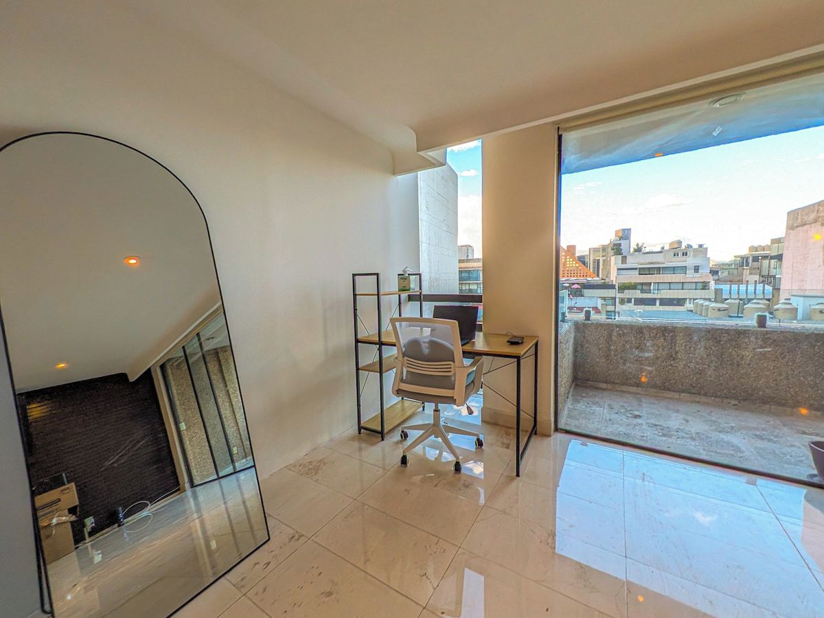 A modern apartment with a balcony, a desk, and a chair.