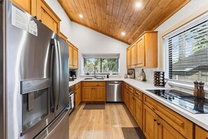 A modern kitchen with wooden cabinets, stainless steel appliances, and a large window providing natural light. - Hot Tub + Big-Screen Theater + Grill Deck | Near Lifts + Trails | Gold Bear (Truckee)