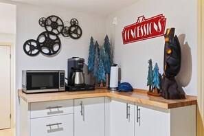 A kitchenette with a microwave, coffee maker, and decorative items including film reels and Christmas trees. - Hot Tub + Big-Screen Theater + Grill Deck | Near Lifts + Trails | Gold Bear (Truckee)