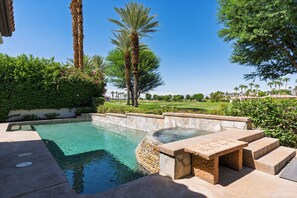A clear swimming pool with stone steps leading into it, surrounded by lush greenery and palm trees. - Pool + Hot Tub + Game Room + Casita | Golf Course Frontage | The Back Nine (La Quinta)