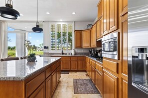 A modern kitchen with wooden cabinets, a stainless steel refrigerator, and a large window with a view of greenery. - Pool + Hot Tub + Game Room + Casita | Golf Course Frontage | The Back Nine (La Quinta)