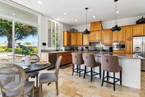 A modern kitchen with wooden cabinets, stainless steel appliances, and a dining area with a table and chairs. - Pool + Hot Tub + Game Room + Casita | Golf Course Frontage | The Back Nine (La Quinta)