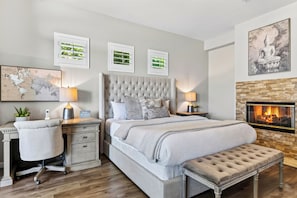 A bedroom with a large bed, a desk, a chair, a map, and a fireplace. - Pool + Hot Tub + Game Room + Casita | Golf Course Frontage | The Back Nine (La Quinta)