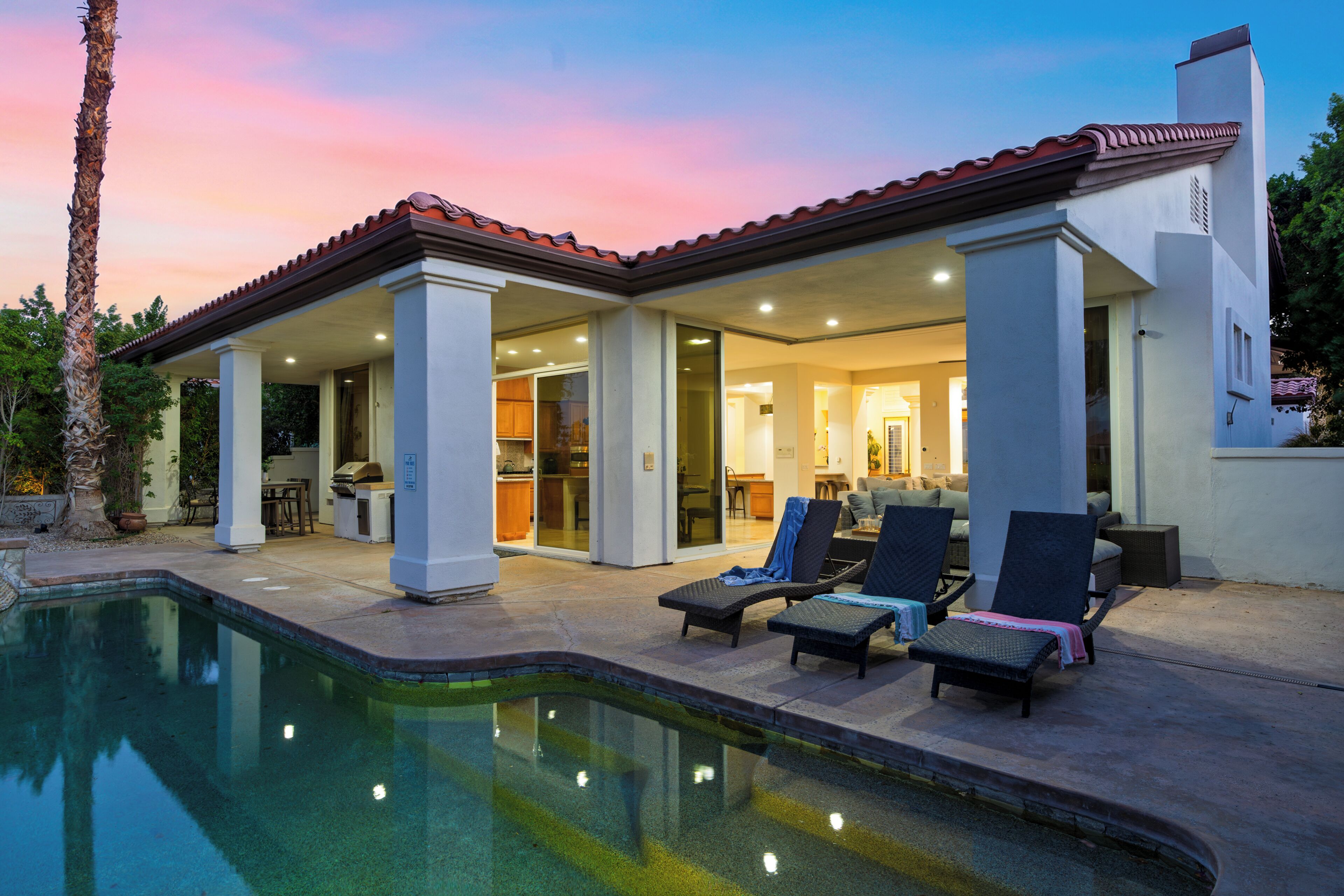 Una casa de dos pisos con piscina, mobiliario exterior y una zona de patio.