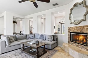 A modern living room with a sectional sofa, a coffee table, a fireplace, and a ceiling fan. - Pool + Hot Tub + Game Room + Casita | Golf Course Frontage | The Back Nine (La Quinta)