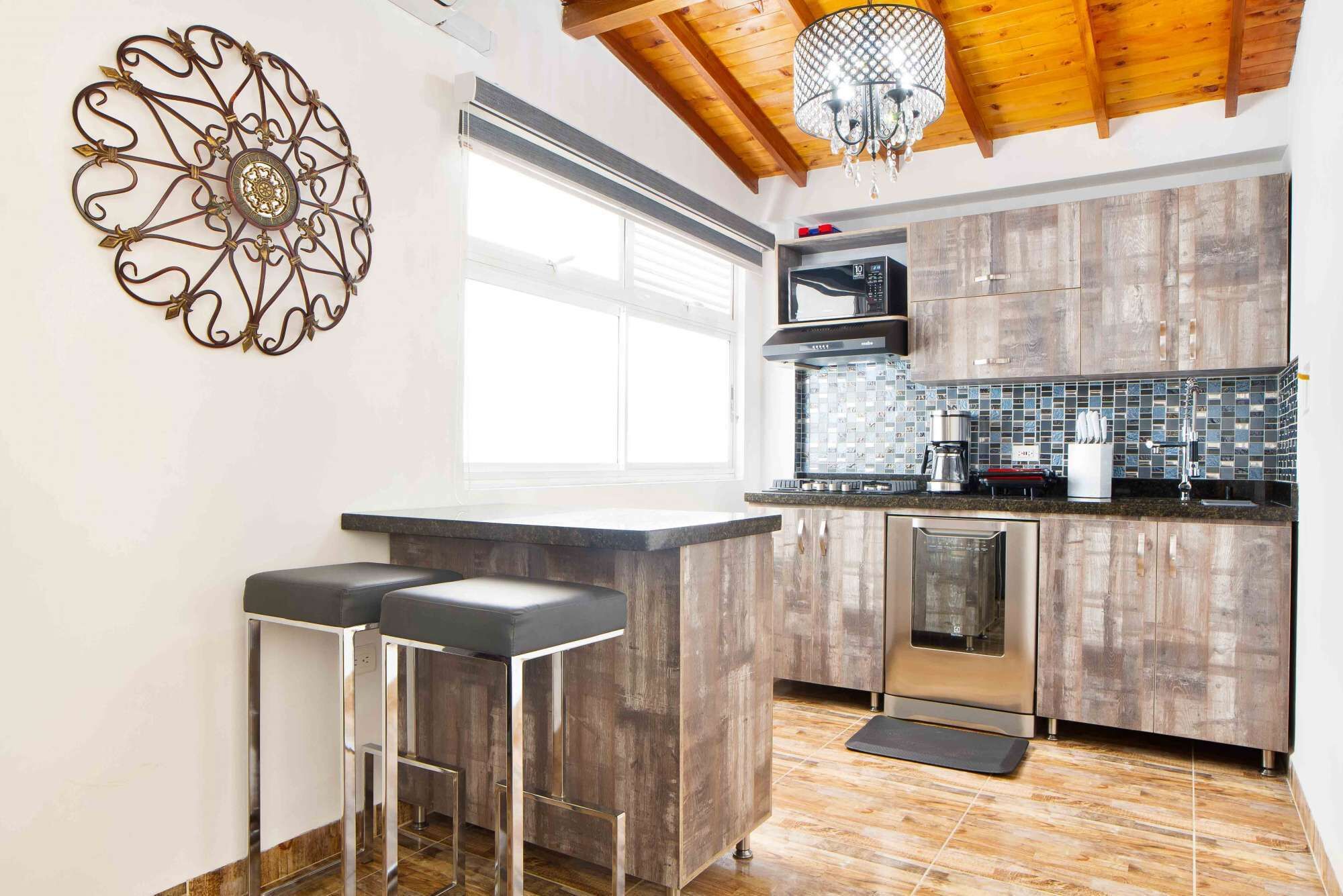 A modern kitchen with wooden cabinets, a stainless steel dishwasher, and a bar area with stools.