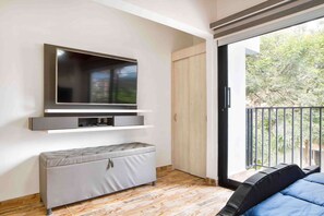 A modern room with a flat-screen TV mounted on the wall, a grey sofa, and a balcony with a view of greenery. - 2 Bedroom Apartment One Hot tub balcony (Medellin)