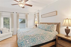 Ein Schlafzimmer mit einem Bett, einem Nachttisch, einer Lampe, einem Deckenventilator und einem Fenster mit Vorhängen.