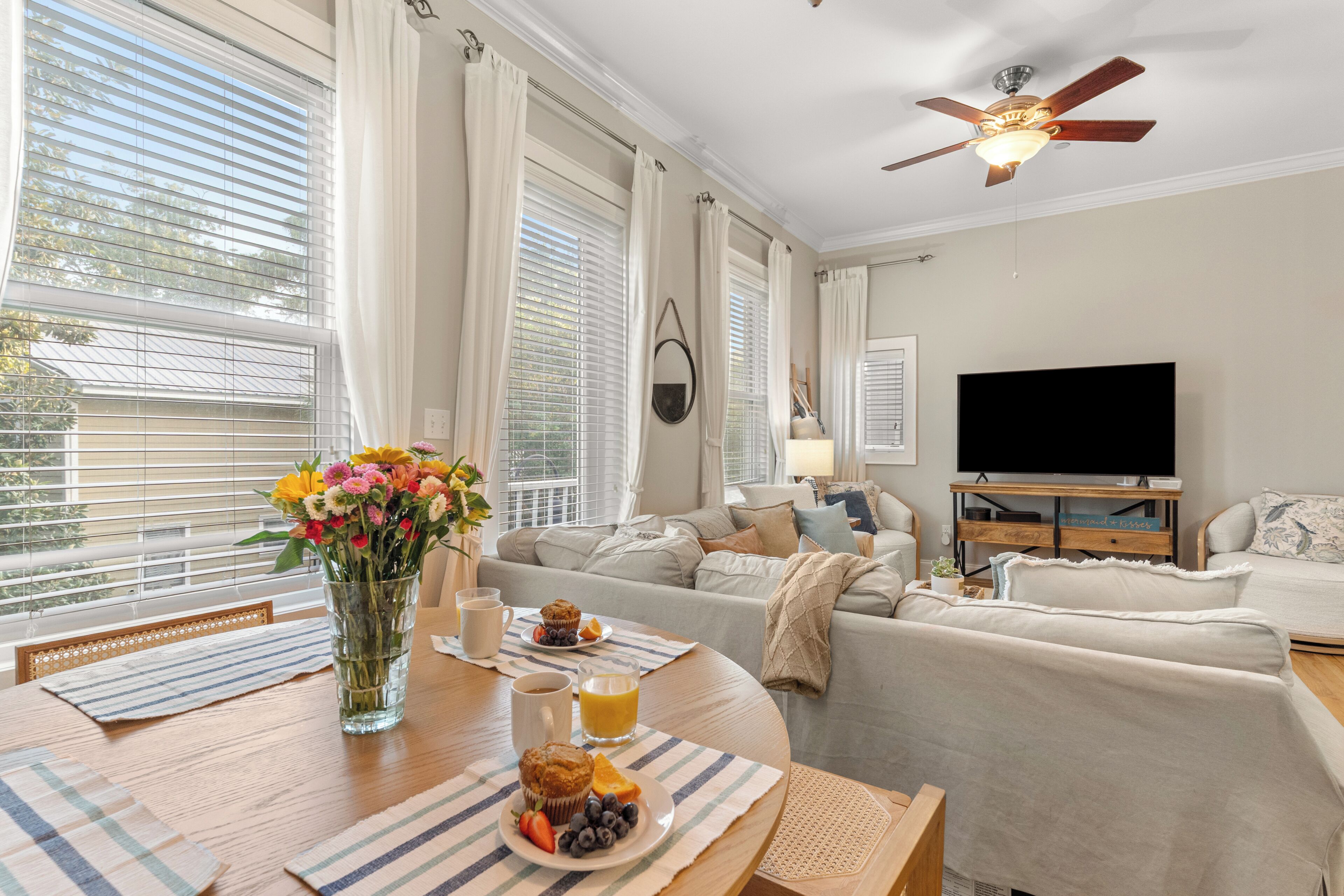 A living room with a sofa, a coffee table with breakfast items, a TV, and a ceiling fan.