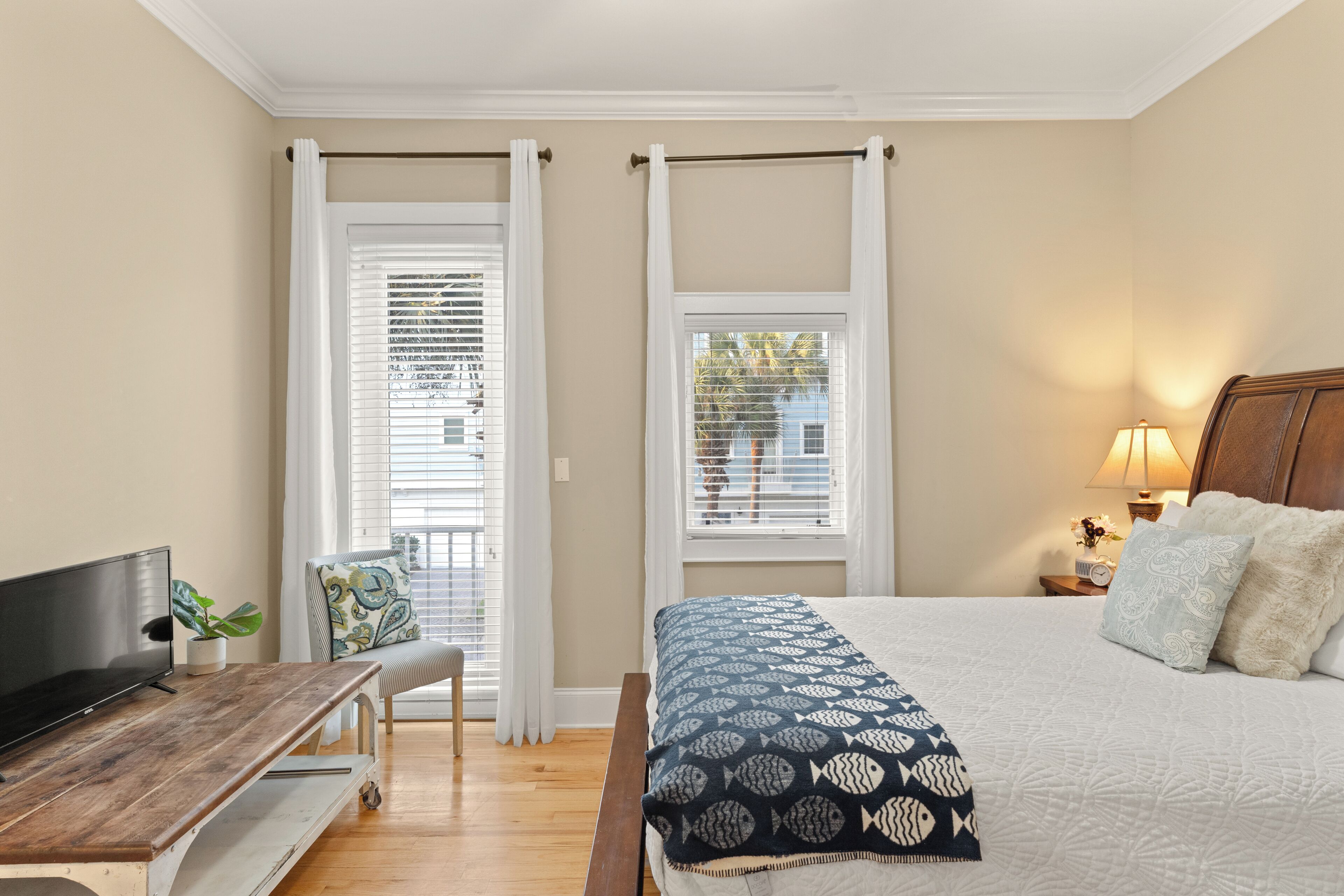 A bedroom with a bed, a TV, a desk, and a window with curtains.