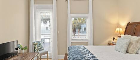 A bedroom with a bed, a TV, a desk, and a window with curtains.