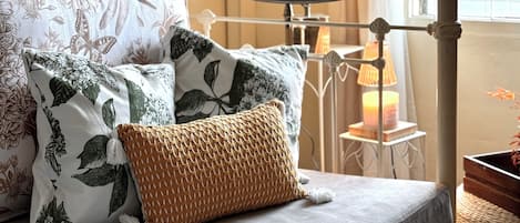 A bed with floral bedding, a woven throw pillow, and a bedside table with a lamp.