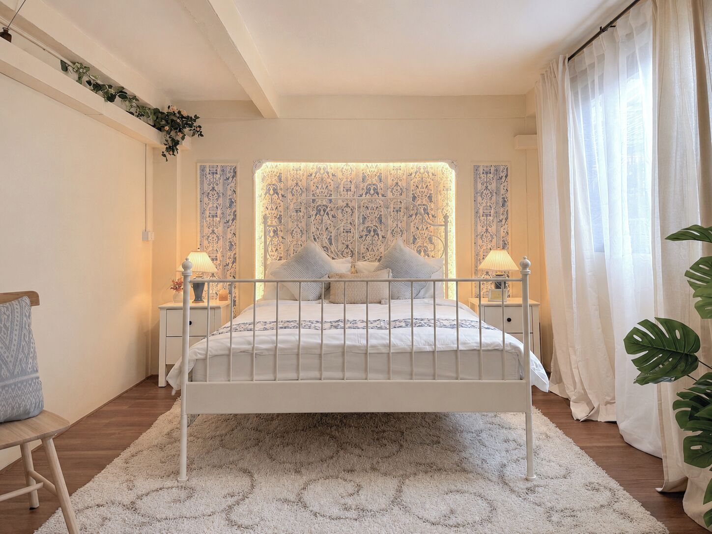 A bedroom with a bed, bedside tables, a nightstand, a chair, and a large window with curtains.