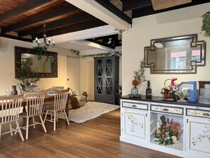 Un coin repas avec des chaises en bois, une table dressée avec des verres et un vase, et un lustre.