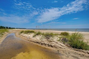 Ein Strand mit blauem Himmel, einem sandigen Pfad zum Wasser und dichter Vegetation.