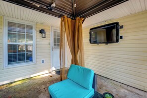 A covered porch with a blue chair, a window with blinds, and a wall-mounted TV. - 1 Mi to Beach! Family-Friendly Waveland Home (Waveland)