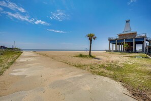 A beach with a concrete path, a palm tree, and a building with a balcony overlooking the ocean. - 1 Mi to Beach! Family-Friendly Waveland Home (Waveland)