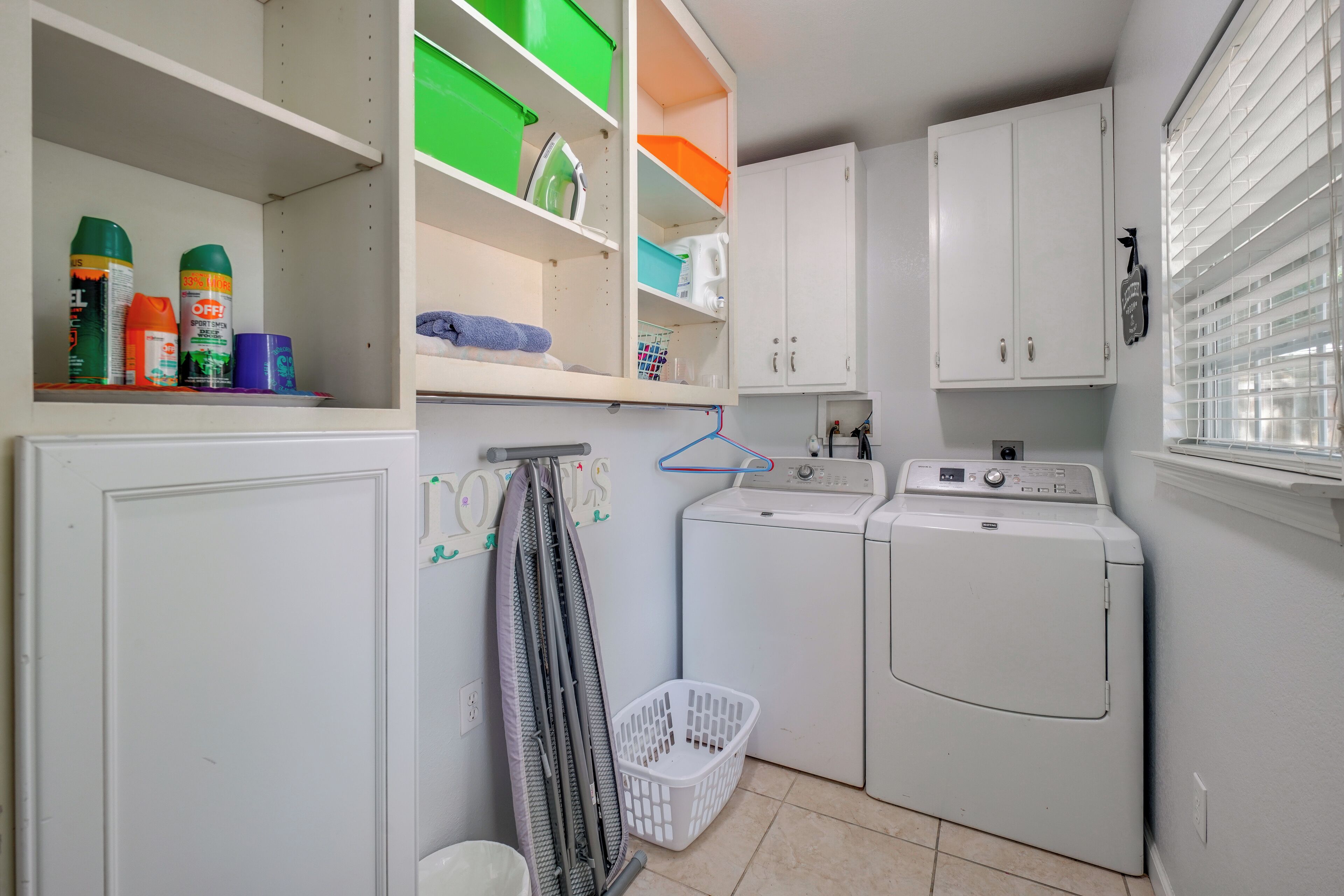 Un cuarto de lavado con lavadora, secadora y repisas con productos de limpieza.