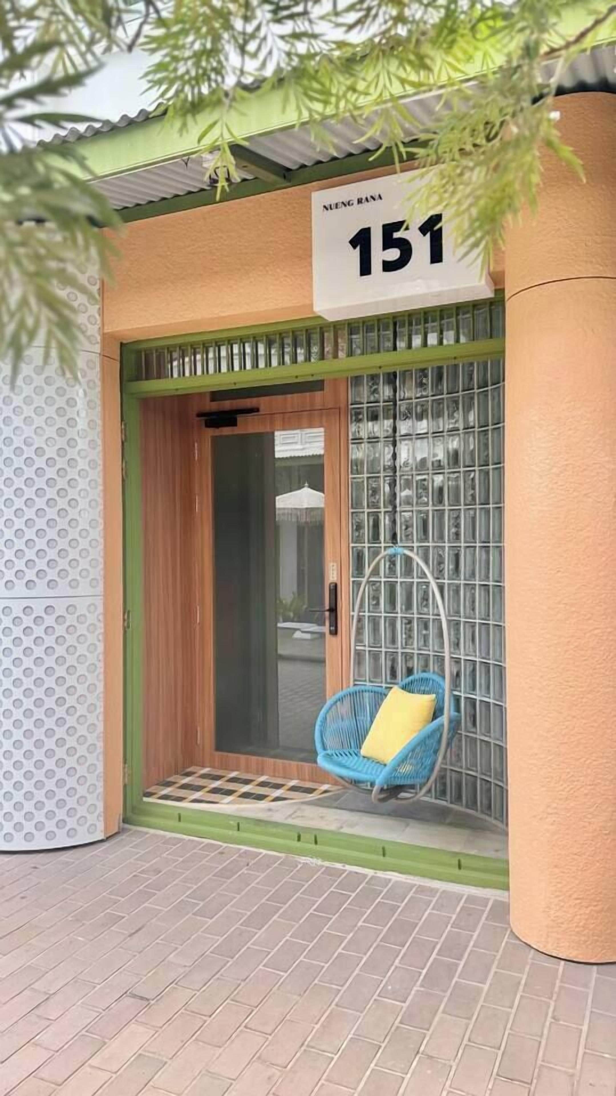 Ein Gebäudeeingang mit Hinweisschild, Glastür, blauem Stuhl und Fliesenboden.