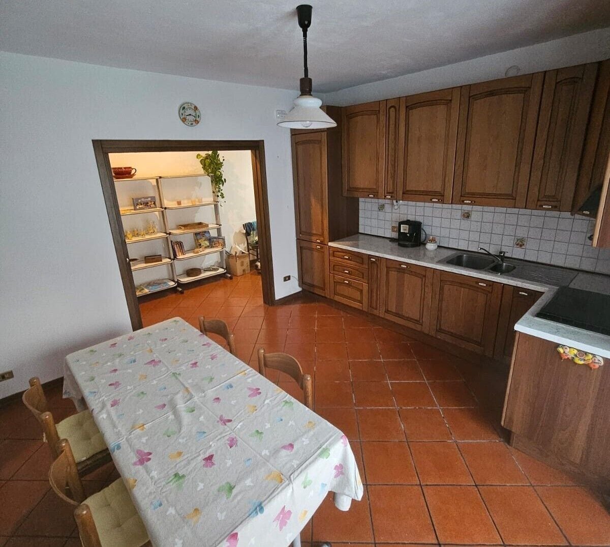 A kitchen with wooden cabinets, a tiled backsplash, a dining table with chairs, and a hanging light fixture.