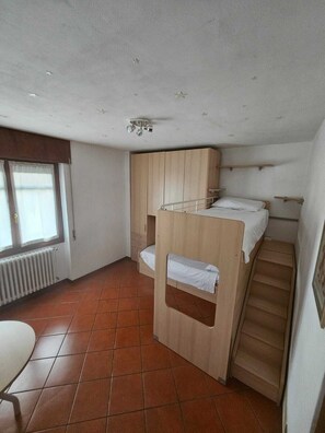A compact room with a bunk bed, a wooden wardrobe, a radiator, and a window with curtains. - Casa Romilda: an apartment just a few meters from the lake, with a garden and ample parking (Lombardia)