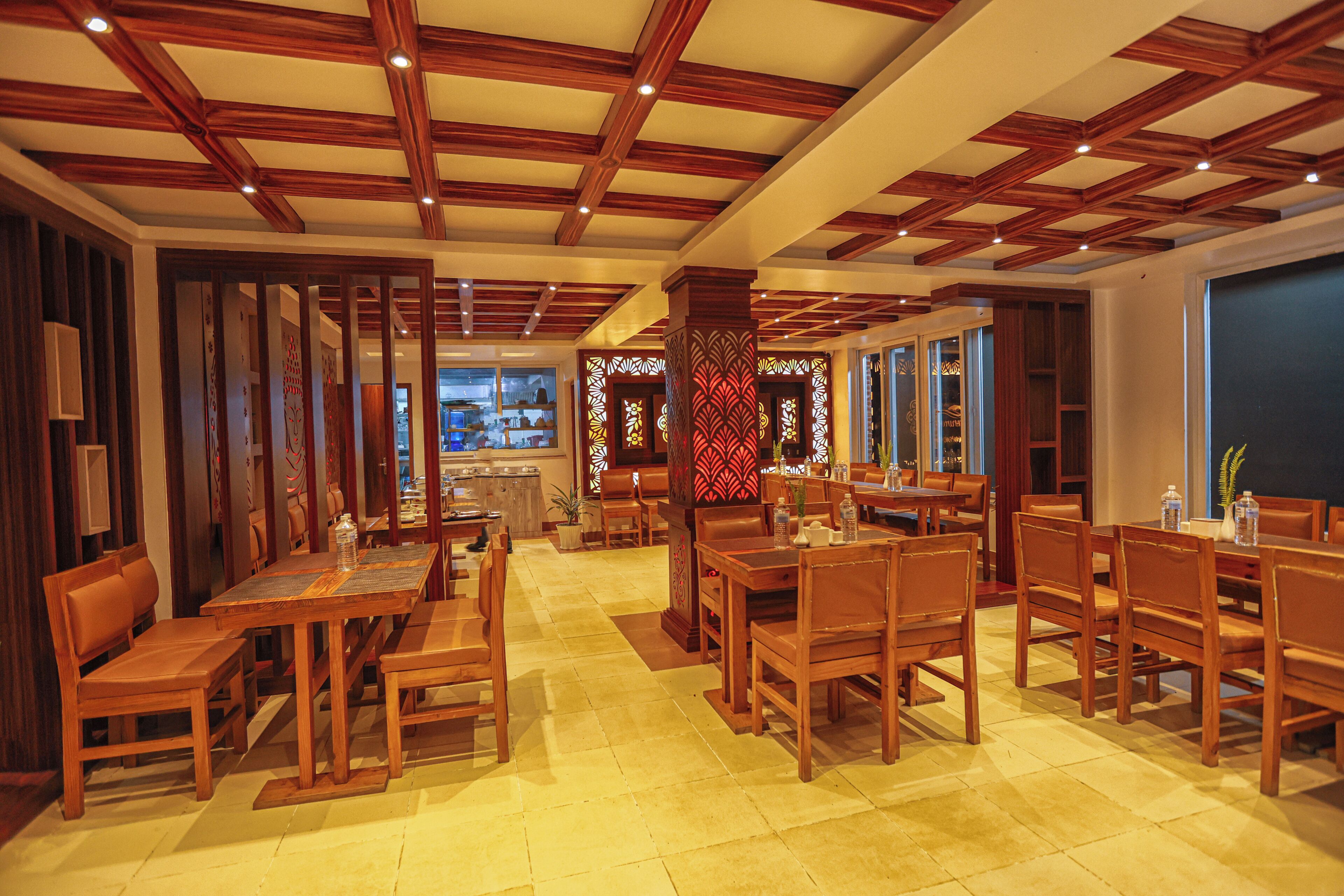 Interior de restaurante con mobiliario de madera, piso de baldosas y cocina visible a través de un separador de vidrio.