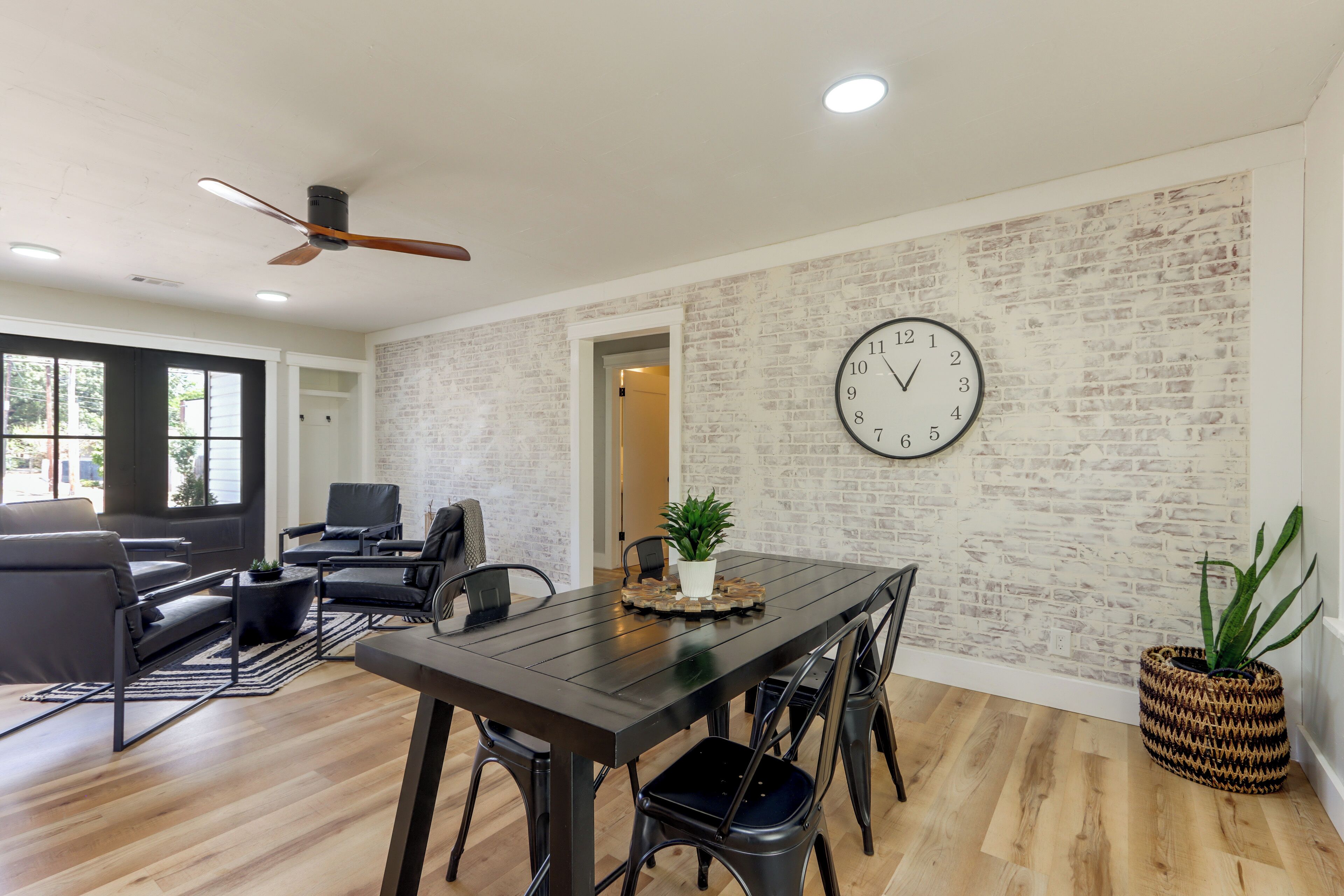 A modern living room with a dark wooden dining table, black chairs, a black sofa, and a brick-patterned wall.
