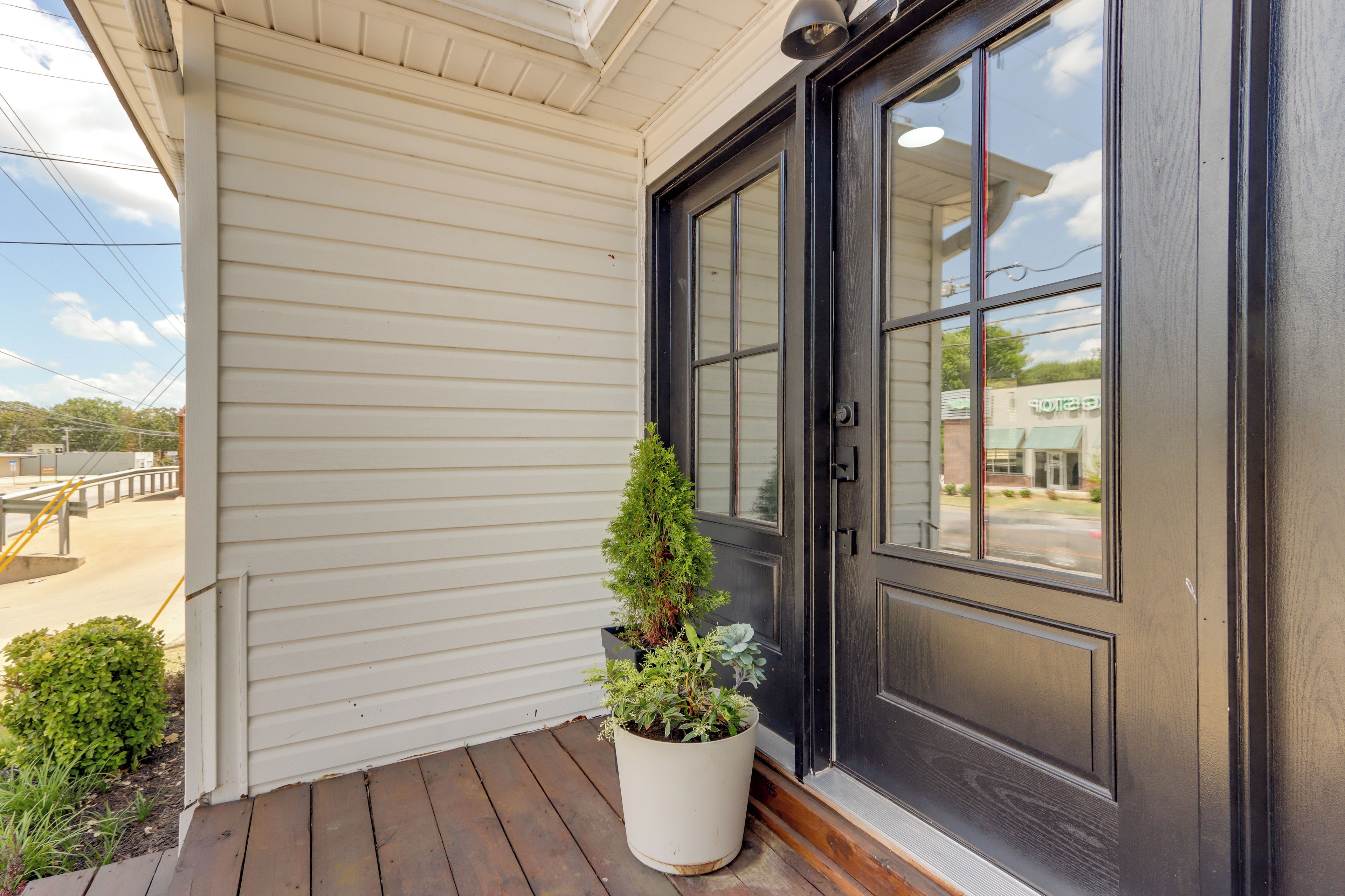 A house's exterior with a dark door, white siding, and a small potted plant on the porch.