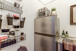 A kitchen with a stainless steel refrigerator, a pegboard with kitchen utensils, and a window above the sink.